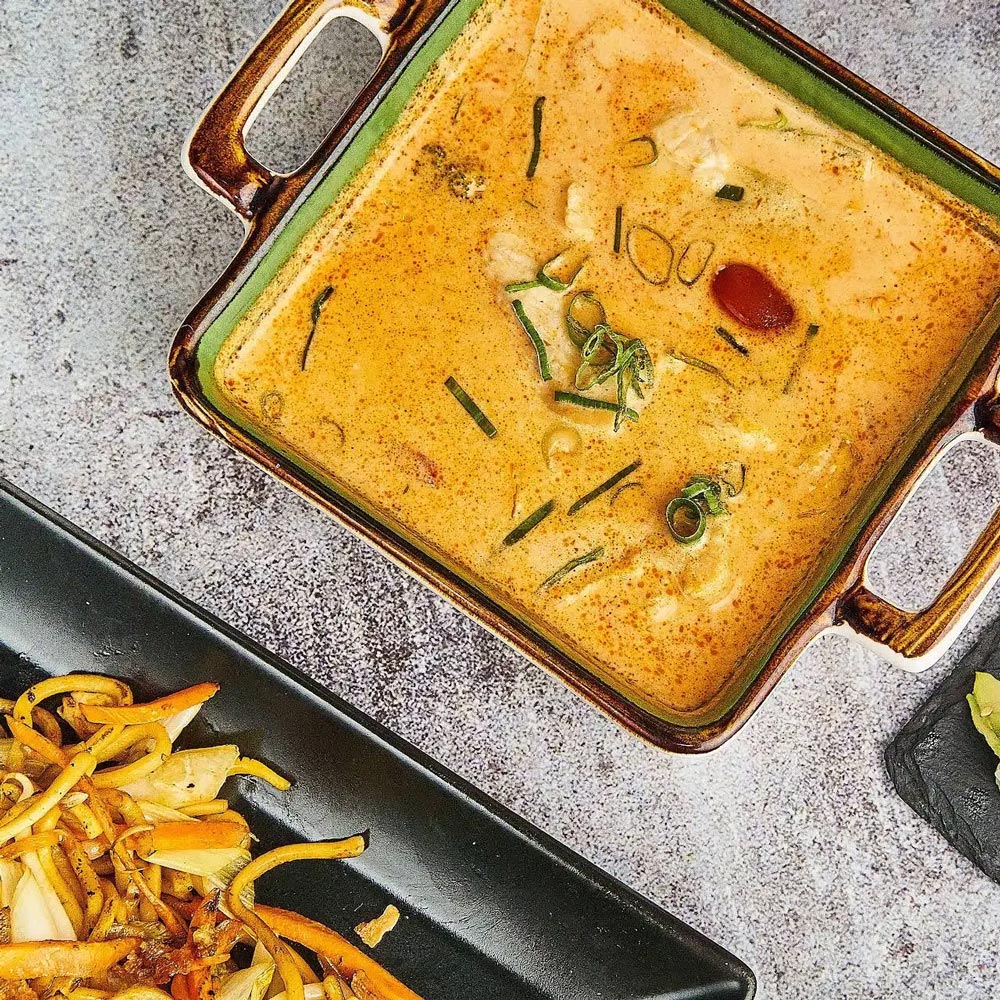 Quadratische Schüssel mit orangefarbener cremiger Suppe und frischen Kräutern